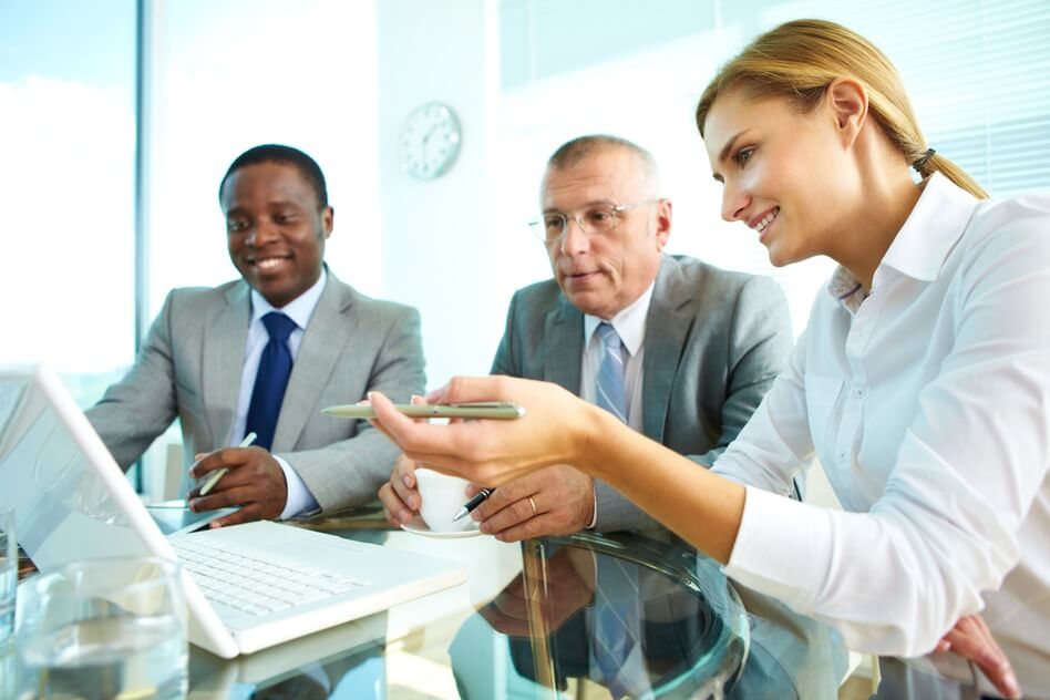 Two men and woman discussing something on a laptop in front of them.