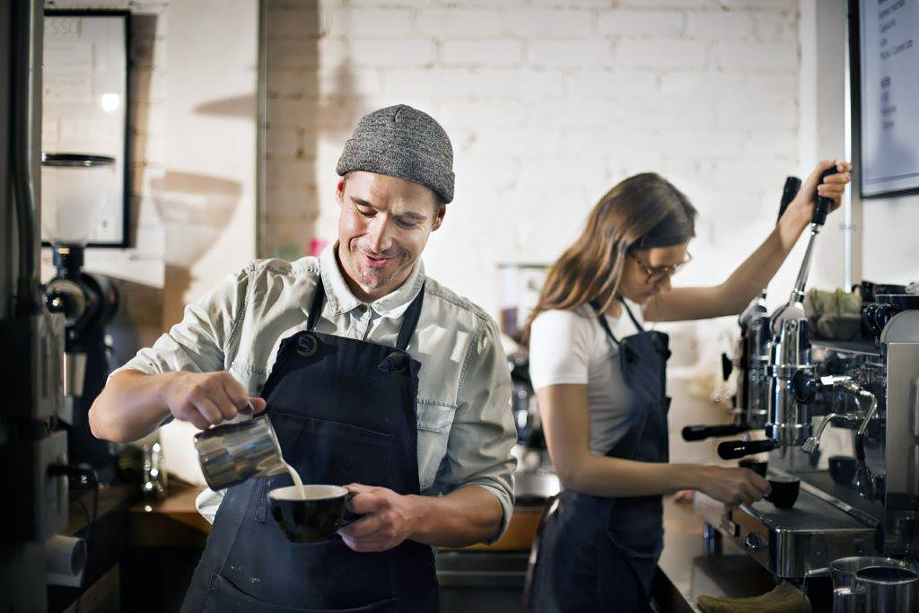 Male and female barristas making and pouring coffee.