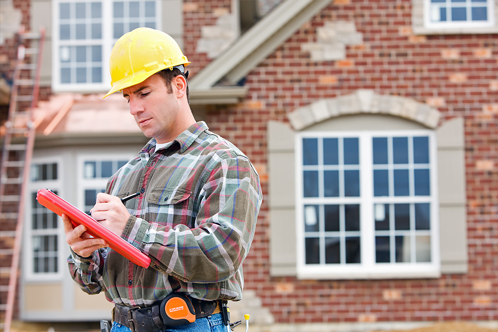 Construction worker taking notes with home in the background.