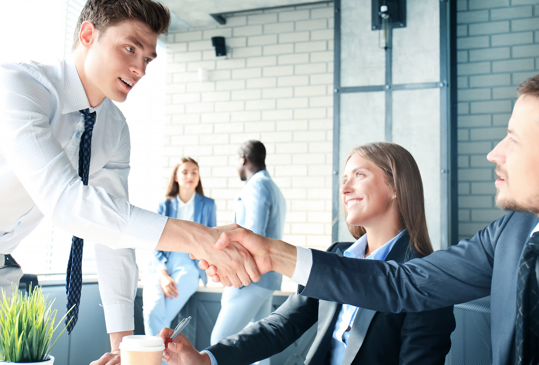 Two business professionals shaking hands as female professional looks on.